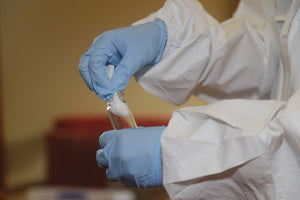 Person in white hazmat suit and blue gloves putting a white cotton swab into a glass vial during an environmental contamination investigation