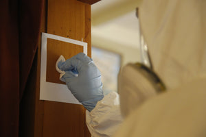 Person in white hazmat suit with blue gloves taking a swab sample in a building for an IANZ accredited meth test