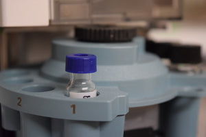 Close up of small glass vial with blue lid in a scientific instrument for laboratory analysis