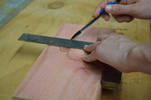 Person holding a ruler on a piece of timber and marking the line to cut with a pencil